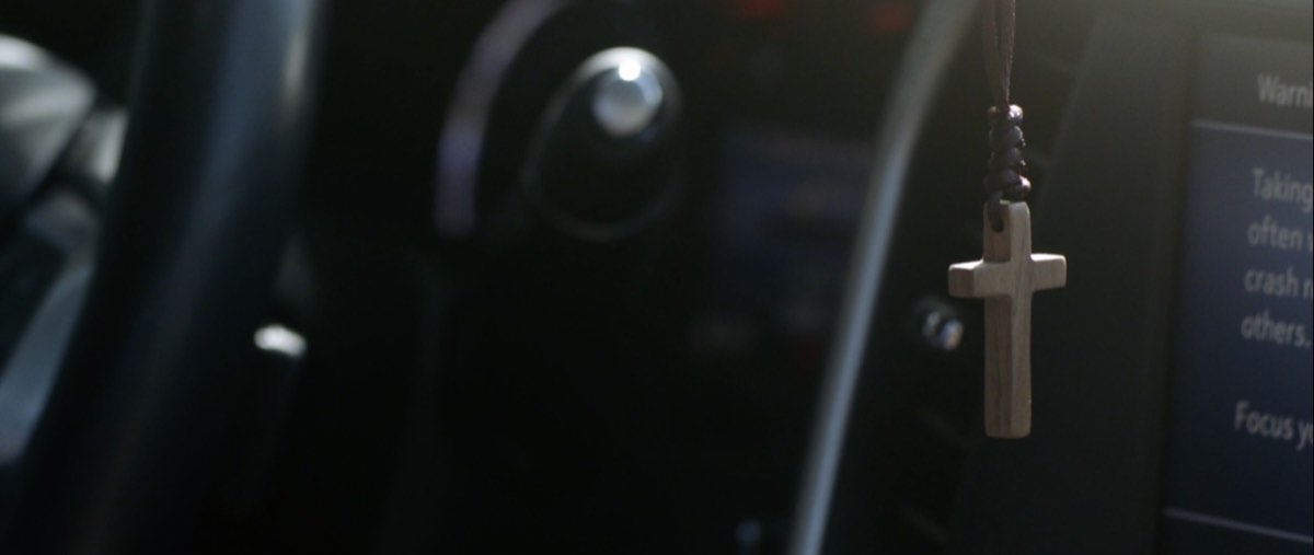 A cross hanging inside a vehicle in a still from Forgiving the Nightmare